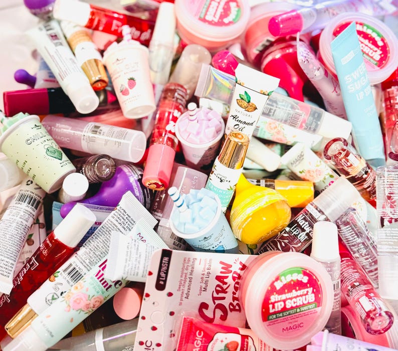 May include: A selection of lip balms, lip scrubs and lip glosses in a range of colours and flavours. The lip balms are in tubes, jars and sticks. The lip scrubs are in jars. The lip glosses are in tubes. The lip balms and lip scrubs have a variety of designs and patterns. The lip glosses are clear, pink and red. The lip balms and lip scrubs are in a variety of colours, including pink, red, blue, green and yellow.