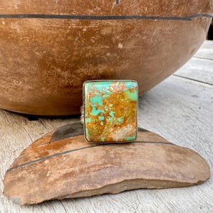 May include: A square turquoise ring with a green and brown stone set in silver.