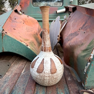 May include: A white ceramic vase with brown accents and a speckled glaze. The vase has a wide, round base and a narrow neck.
