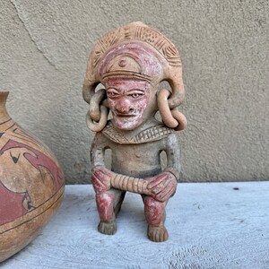 May include: A terracotta figurine of a person with a headdress and intricate details. The figurine is painted in shades of red and brown.