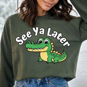 K&ouml;nnte beinhalten: Ein gr&uuml;ner Pullover mit einem Karikatur-Alligator und dem Text "See Ya Later" in Wei&szlig;.