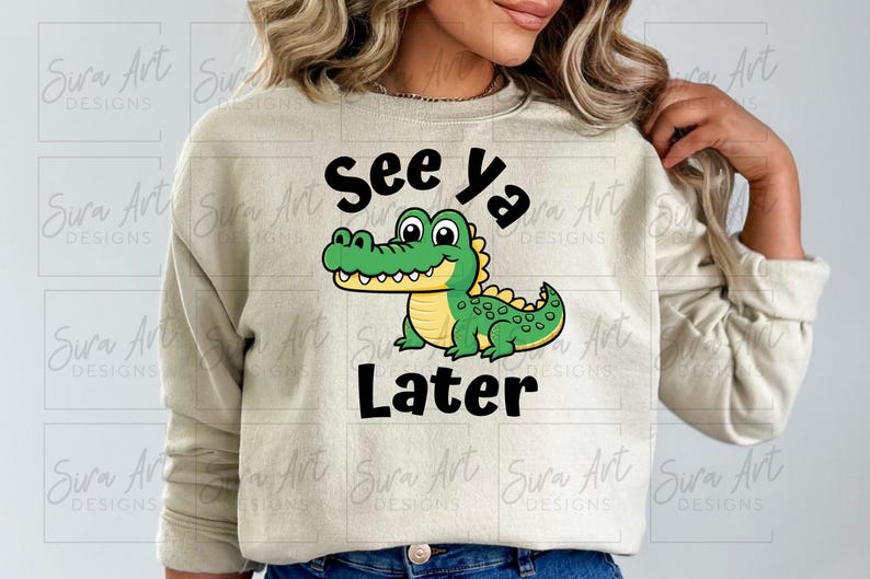 K&ouml;nnte beinhalten: Ein hellbeiger Pullover mit einem gr&uuml;nen Alligator-Cartoon-Motiv und dem Text "See ya Later" in Schwarz.