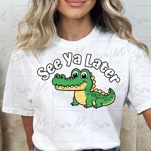 K&ouml;nnte beinhalten: Wei&szlig;es T-Shirt mit einem gr&uuml;nen Comic-Alligator und dem Text "See ya Later" in Schwarz.