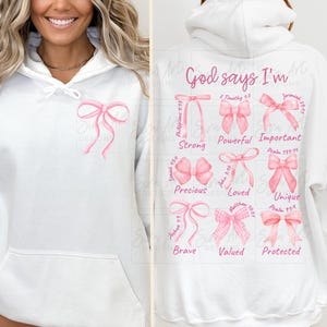 May include: White hoodie with a pink bow on the front and a design on the back that says "God says I'm" with pink bows and bible verses.