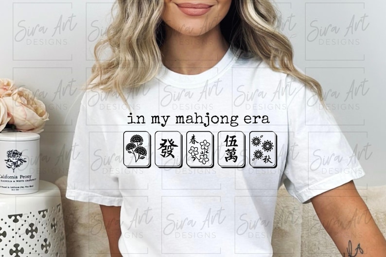 May include: White t-shirt with the phrase "in my mahjong era" and five black and white mahjong tiles. The tiles feature various symbols. A casual, comfortable top for game enthusiasts.