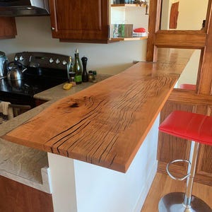 Peut inclure: Un plan rapproché d'un comptoir en bois avec un motif de grain de bois naturel. Le comptoir est de couleur brun clair avec des stries brun foncé. Le comptoir est dans un environnement de cuisine et fait partie d'un bar ou d'un coin repas.