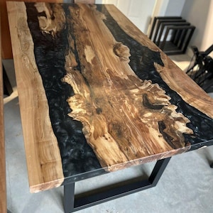 May include: A large wooden table with a black epoxy resin inlay. The table has a natural wood finish and a black metal base.