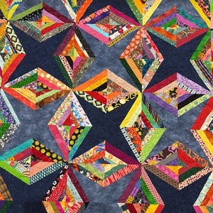 May include: A colorful quilt with a geometric design. The quilt features diamond shapes in various sizes, each composed of strips of fabric in a variety of colors and patterns, including red, orange, green, and blue. The background is a dark blue fabric.