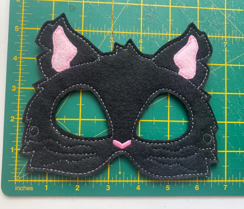 May include: Black felt cat mask with pink felt ears and eye holes. The mask is approximately 6 inches wide.
