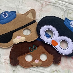May include: Three felt animal masks for children. A brown cat mask with a blue hat and eye patch, a brown bear mask with green accents, and a black and white penguin mask with a blue hat.