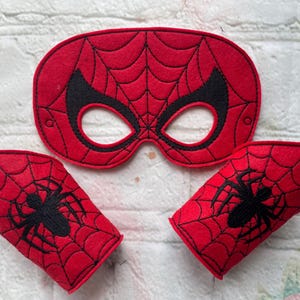 May include: Red felt mask with a black spider web design and eye holes. Two red felt wrist cuffs with black spider web designs and a black spider silhouette.