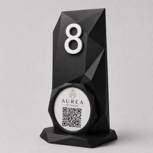 Op de afbeelding: Zwarte geometrische tafelnummerhouder met een wit nummer 8. De houder heeft een cirkelvormige uitsparing met de tekst "Aurea Bistro" en een QR-code. Het ontwerp is modern en hoekig.
