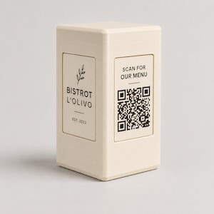 Puede incluir: Un expositor de mesa rectangular blanquecino con el texto "BISTROT L'OLIVO EST. 2022" y un código QR que dice "SCAN FOR OUR MENU". El diseño es minimalista.