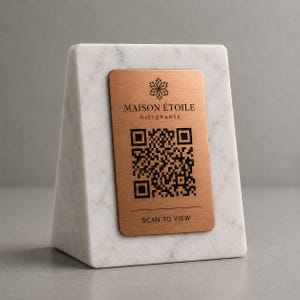Può includere: Un blocco di marmo bianco con una placca metallica color rame. La placca presenta un codice QR e il testo "MAISON ÉTOILE RISTORANTE" e "SCAN TO VIEW". Il marmo ha venature grigie.