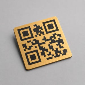 Può includere: Un codice QR quadrato color oro su sfondo quadrato. Il codice QR è nero e riempie la maggior parte del quadrato. Lo sfondo è grigio chiaro.