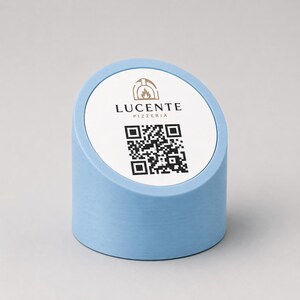 Pode incluir: Um suporte azul claro com a parte superior inclinada, com o texto "LUCENTE PIZZERIA" e um código QR. O suporte tem uma base cilíndrica e uma parte superior circular branca com o logotipo da pizzaria. O fundo é de cor neutra.