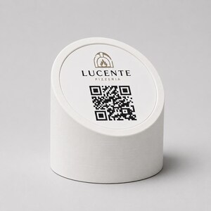 Peut inclure: Un présentoir de table cylindrique blanc avec un dessus incliné. Le dessus présente le texte "LUCENTE PIZZERIA" et un code QR. Un logo de four à pizza est au-dessus du texte. Le présentoir est conçu pour être posé sur une table.