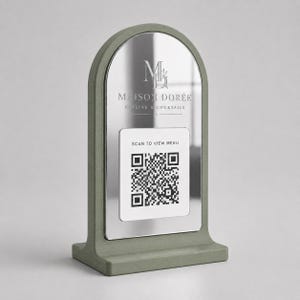 Può includere: Un cartello da tavolo verde salvia con una parte superiore ad arco in metallo argentato. Il cartello recita "MAISON DORÉE CUISINE & COCKTAILS" e include un codice QR con il testo "SCAN TO VIEW MENU".