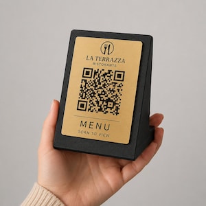 Może przedstawiać: Czarny uchwyt na menu stołowe ze złotą kartą. Karta zawiera tekst "LA TERRAZZA RISTORANTE", kod QR oraz słowo "MENU" z napisem "SCAN TO VIEW" poniżej. Uchwyt jest ustawiony pod kątem ułatwiającym przeglądanie.