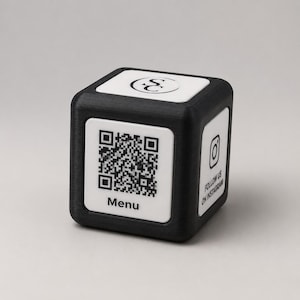 Könnte beinhalten: Ein schwarzer Würfel mit weißen Tafeln. Eine Tafel zeigt einen QR-Code und das Wort "Menu". Eine andere hat das Instagram-Logo und den Text "Follow us on Instagram". Die obere Tafel hat ein Logo.
