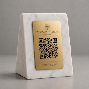 Può includere: Un supporto per codice QR in marmo con una placca metallica color oro. La placca presenta il testo "MAISON ÉTOILE RISTORANTE" e "SCAN TO VIEW" insieme a un codice QR. Il supporto in marmo ha un motivo venato bianco e grigio.