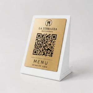 Può includere: Un porta menu da tavolo bianco con una placca color oro. La placca presenta un codice QR e il testo "LA TERRAZZA RISTORANTE" e "MENU SCAN TO VIEW". Il supporto è angolato per una facile visualizzazione.