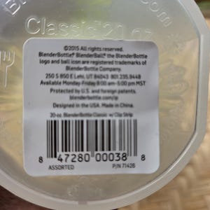 May include: A clear BlenderBottle Classic with a 591 ml capacity. The bottle has a white label with black text, including the BlenderBottle logo and product information. Designed in the USA, made in China.