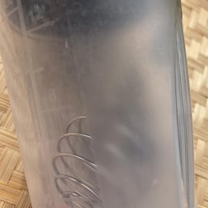 K&ouml;nnte beinhalten: Eine transparente Kunststoff-Shakerflasche mit Messmarkierungen. Im Inneren der Flasche befindet sich ein silberner Drahtquirl. Die Flasche ist teilweise mit einer tr&uuml;ben Fl&uuml;ssigkeit gef&uuml;llt. Der Hintergrund ist eine Oberfl&auml;che aus geflochtenem Bambus.