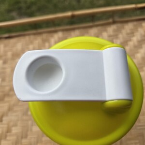 May include: A close-up of a yellow and white water bottle lid. The lid is bright yellow with a white flip-top closure. The closure has a circular opening. The background is a woven bamboo mat.