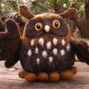 以下が含まれることがあります： 白とオレンジの斑点のある茶色と黒のフェルトのフクロウ。フクロウは大きく丸いオレンジ色の目を持っている。