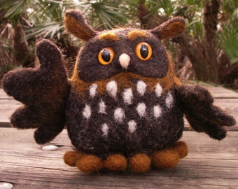 May include: A brown and black felt owl with white spots and orange feet. The owl has large, round, orange eyes.