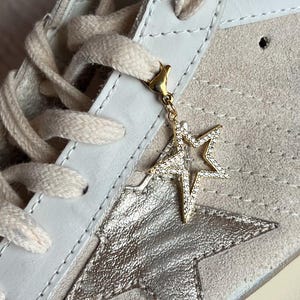 May include: White suede high-top sneakers with a silver star on the side and a gold star charm attached to the laces.