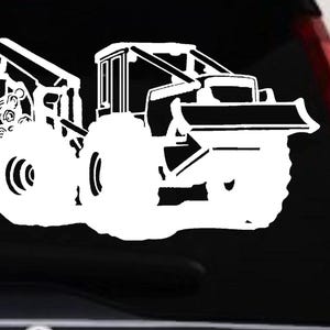May include: A white vinyl decal featuring a detailed silhouette of a forestry skidder machine. The graphic depicts the heavy-duty vehicle with large treaded tires, a front blade, and a rear grapple arm actively clutching a bundle of harvested logs.