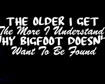 May include: A black graphic design featuring white text that reads: THE OLDER I GET The More I Understand WHY BIGFOOT DOESN'T Want To Be Found. The lettering is presented in a bold, stylized font against a solid black background.