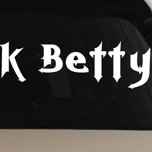 May include: White vinyl decal with the words "Black Betty" in a gothic font. The decal is designed to be applied to a car window or other smooth surface. The text is centered and clearly visible against a black background.