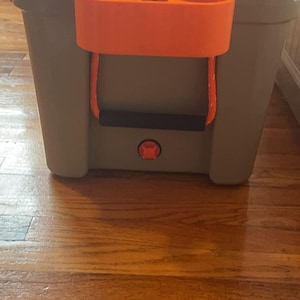 May include: A gray cooler with an orange cup holder and a black handle. The cooler has a red button on the front.