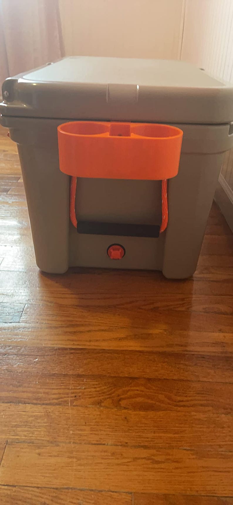 May include: A gray cooler with an orange cup holder and a black handle. The cooler has a red button on the front.