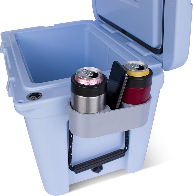 May include: A blue cooler with a gray drink holder that has two cans and a phone in it.