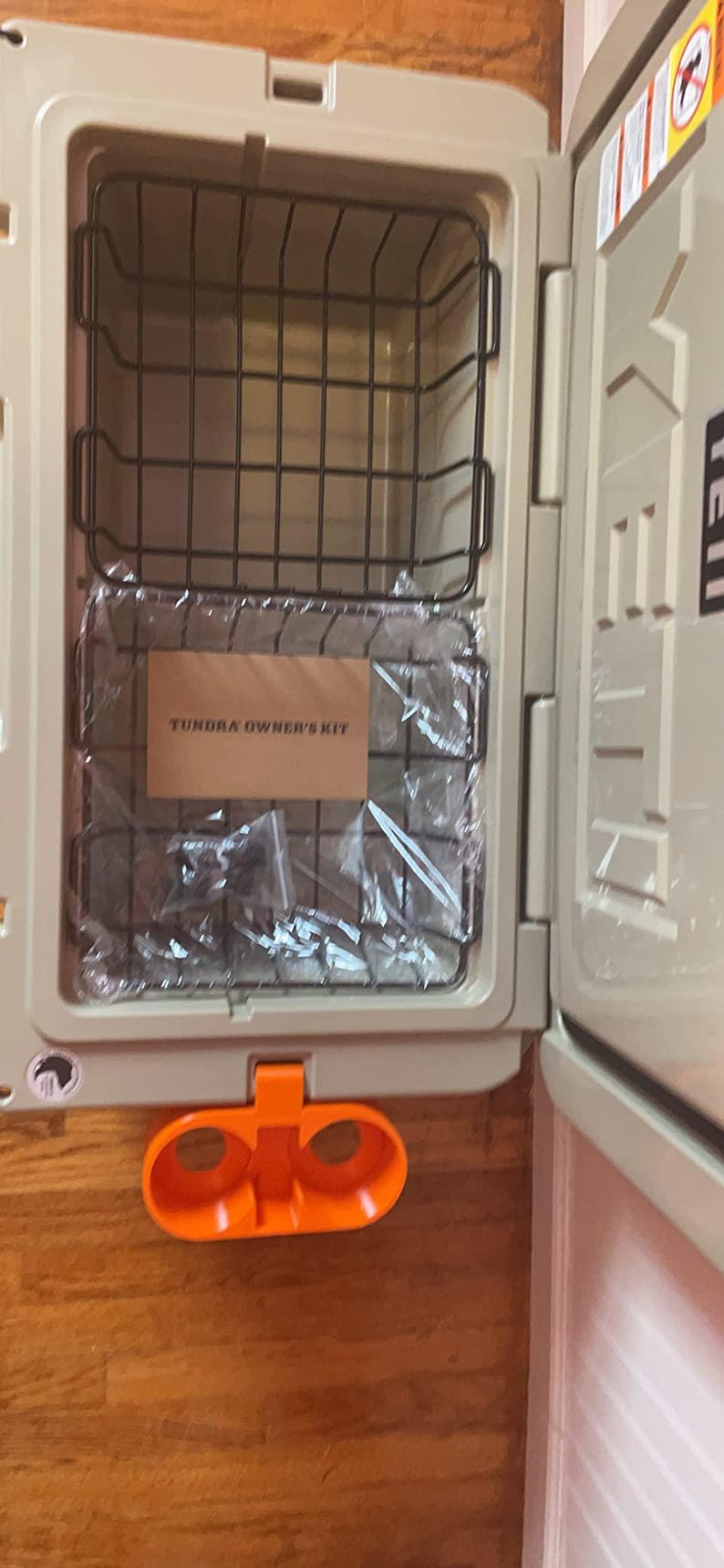 May include: A beige cooler with a black wire basket inside. The cooler has a label that says "Tundra Owner's Kit". The cooler has an orange cup holder on the bottom.