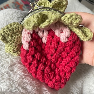 May include: A crocheted strawberry-shaped coin purse with a green crocheted leaf design and a silver clasp.