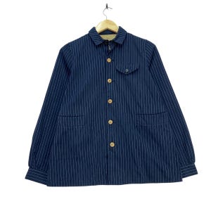 May include: A navy blue long-sleeve jacket featuring a white pinstripe pattern, a standard collar, and a button-down front with light-colored wooden buttons. The jacket includes a single chest pocket with a flap and two lower front pockets.