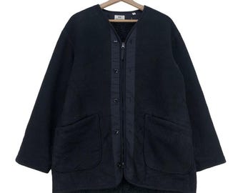 Puede incluir: Chaqueta acolchada azul marino oscuro con cuello en V, mangas largas y dos bolsillos delanteros grandes. La chaqueta presenta cierre de botones y cremallera, con un panel central de tela azul marino oscuro en contraste.