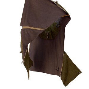 May include: A brown and olive green garment with a hood and a pocket. The garment has a zipper and buttons. The hood is open, revealing the interior lining. The garment appears to be made of a durable fabric.