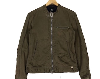 May include: Olive green jacket with a stand-up collar, a full-length zipper, and multiple pockets. The jacket is hanging on a wooden hanger. The jacket has a small pocket on the chest and two pockets on the lower front. The jacket has a small tag on the lower right side.