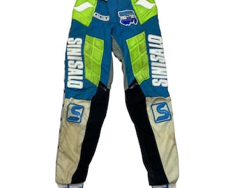 Op de afbeelding: Blauwe, witte, zwarte en neon groene racebroek met het woord "SINISALO" verticaal op de zijkanten gedrukt. De broek heeft gewatteerde delen en een logopatch. De manchetten hebben een klein vlagontwerp.