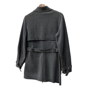 May include: A gray coat with a notched collar, a belt at the waist, and button details. The coat has long sleeves with buttoned cuffs and a back vent. It is hanging on a wooden hanger against a white background.