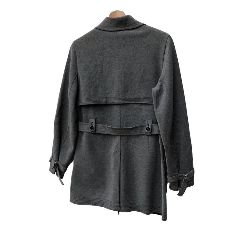 May include: A gray coat with a notched collar, a belt at the waist, and button details. The coat has long sleeves with buttoned cuffs and a back vent. It is hanging on a wooden hanger against a white background.
