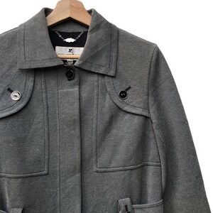 May include: A gray coat with a notched collar, two front pockets, and decorative buttons. The coat is hanging on a wooden hanger. The coat has a tailored fit and a classic design.