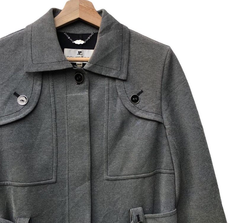 May include: A gray coat with a notched collar, two front pockets, and decorative buttons. The coat is hanging on a wooden hanger. The coat has a tailored fit and a classic design.