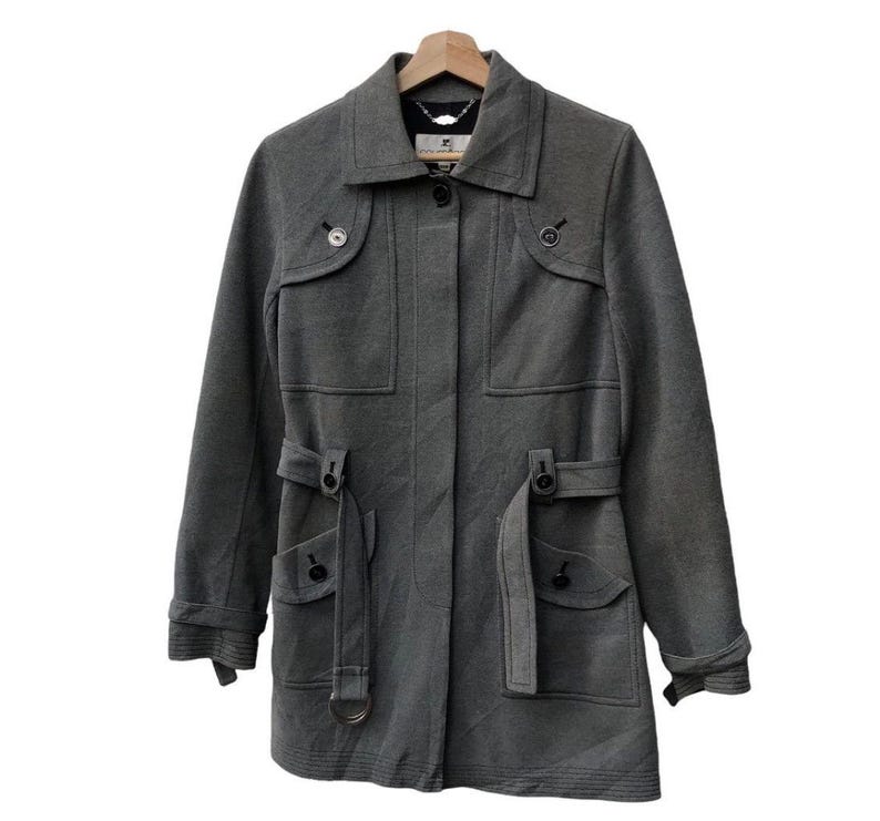 May include: A gray, long-sleeved coat with a collared neckline and button closures. The coat features two front pockets with flaps, belt loops, and a matching belt. The coat is hanging on a wooden hanger.